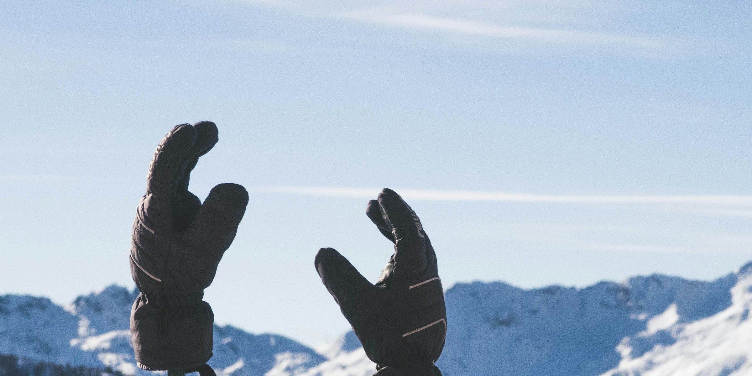 Zwei Ski- und Winterhandschuhe auf Skistöcken vor verschneiten Berggipfeln