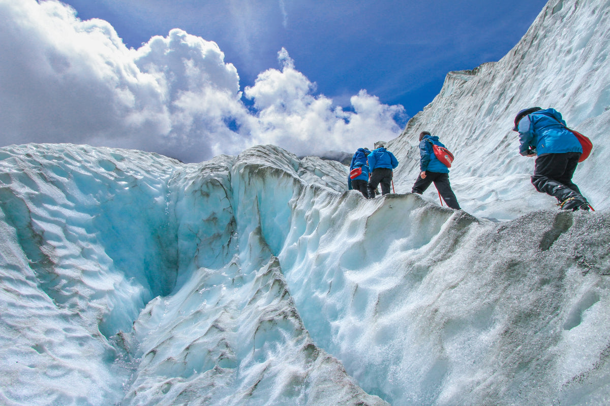 Bergsteiger mit Helm und Rucksack steigen über blau schimmerndes Gletschereis
