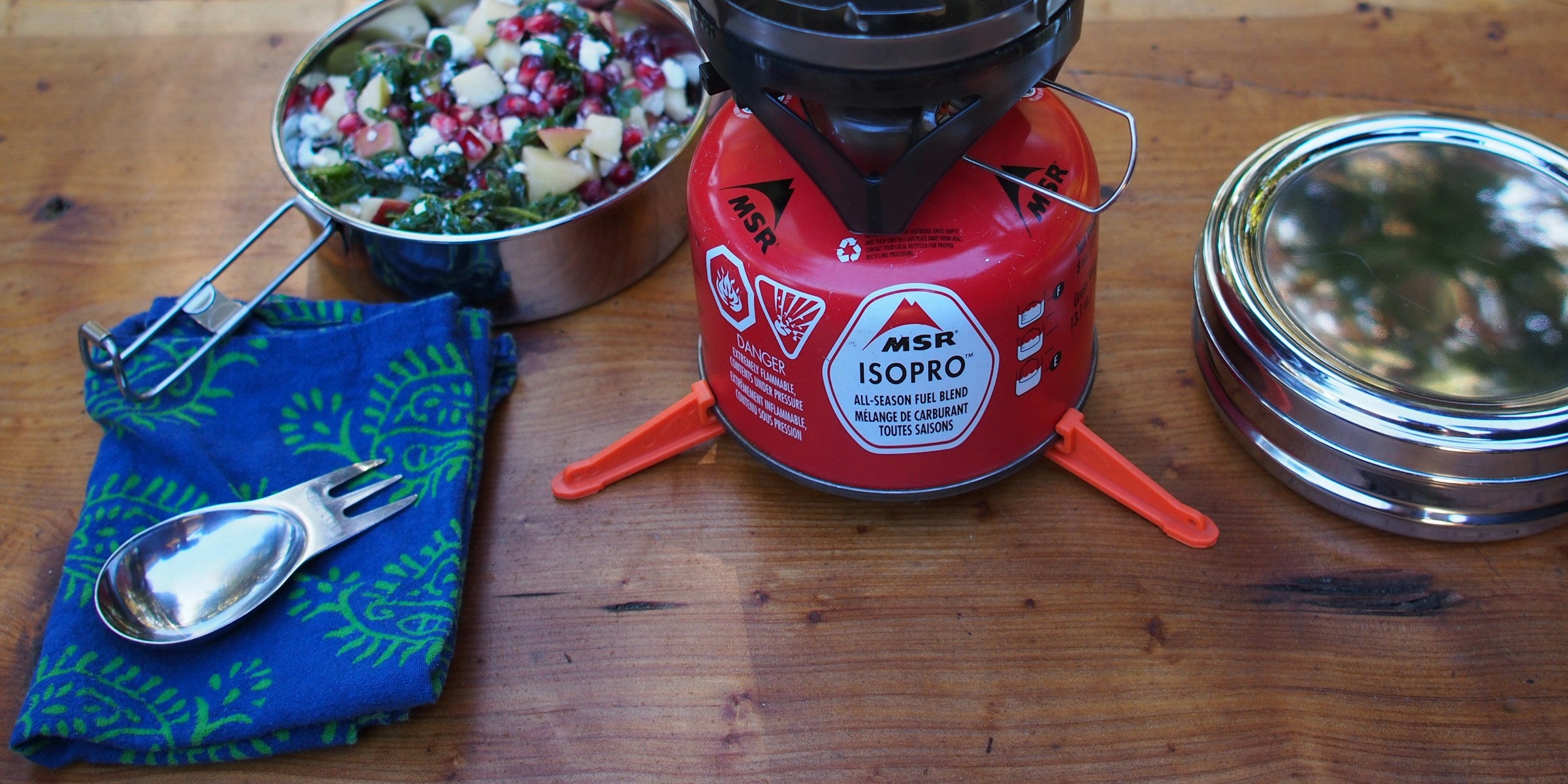 Kochen im Freien mit Gaskocher, Topf und Campingbesteck auf einem Holztisch