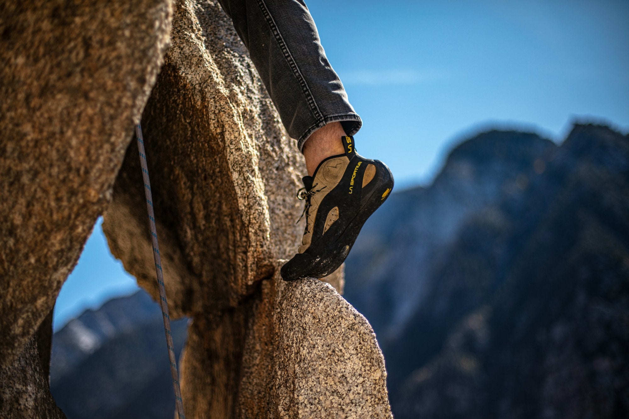 Kletterschuh auf einem Granitfelsen vor Bergen und blauem Himmel