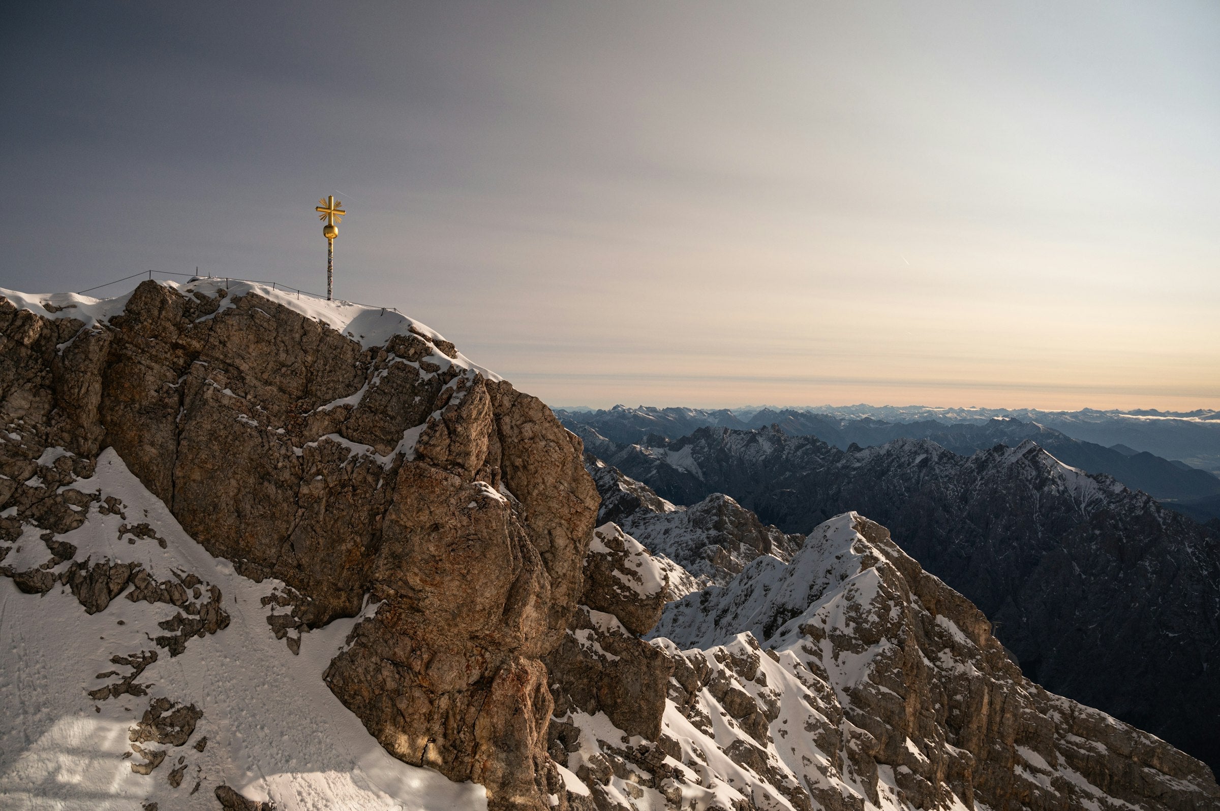 Bergsteiger am goldenen Gipfelkreuz der Zugspitze im Abendlicht, dahinter die Gipfel des Wettersteingebirges