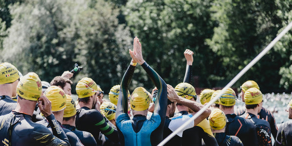 Triathleten mit Badekappen und Neoprenanzügen warten am Ufer auf den Schwimmstart