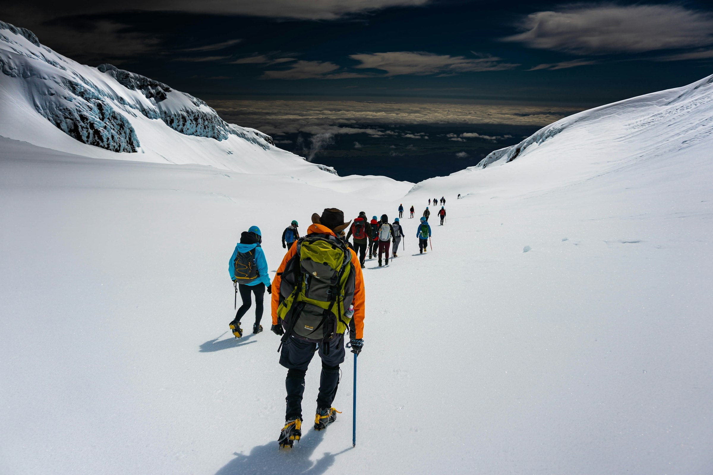 Gruppe von Bergsteigern mit Helm und Rucksack steigt über einen verschneiten Gletscherhang im Hochgebirge auf