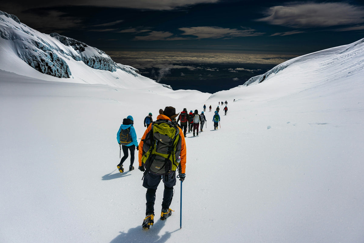 Gruppe von Bergsteigern mit Helm und Rucksack steigt über einen verschneiten Gletscherhang im Hochgebirge auf
