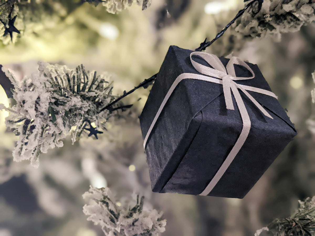 Verpacktes Geschenk mit Schleife hängt an einem verschneiten Tannenzweig