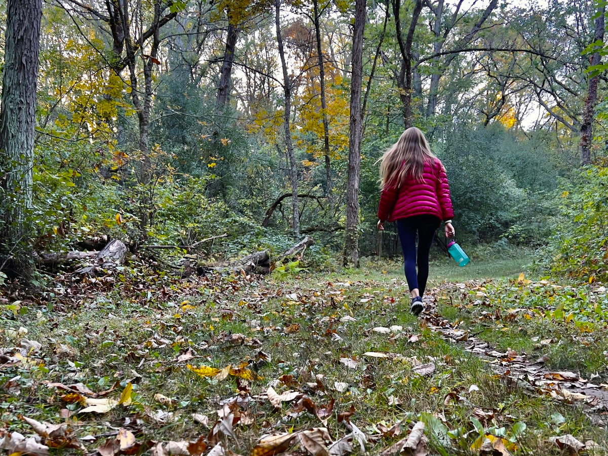 Wanderin mit roter Jacke auf einem Waldweg im Herbst