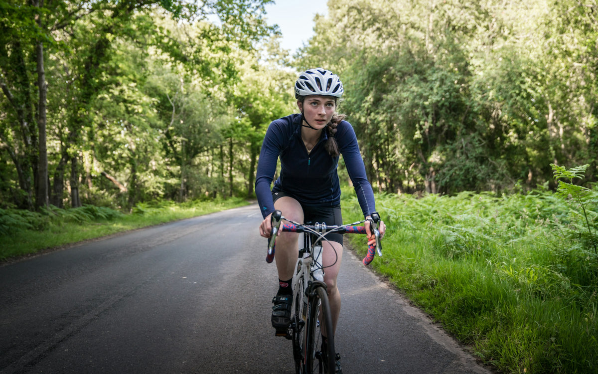 Radfahrerin mit weißem Fahrradhelm auf einer Landstraße im Grünen