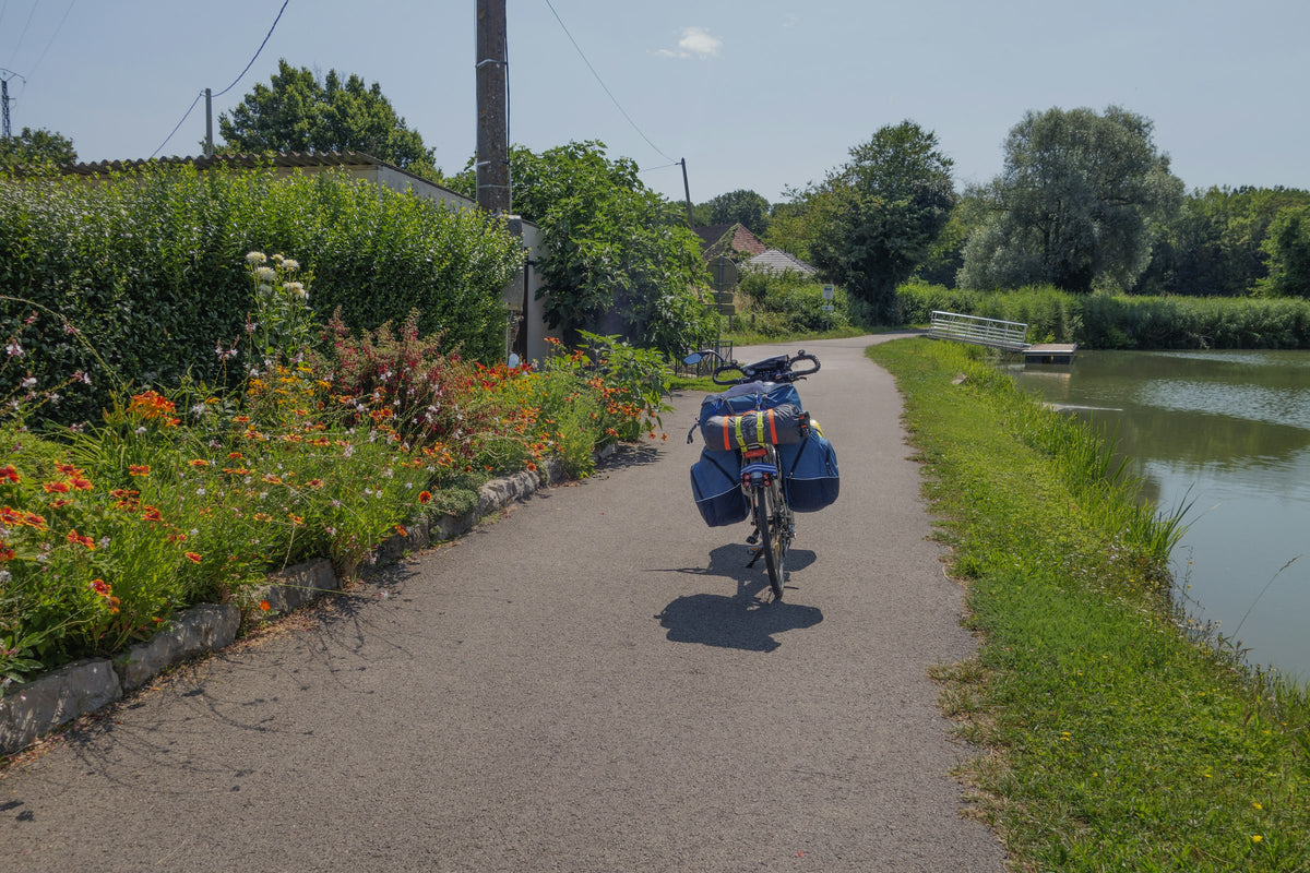 Radreisender mit Packtaschen auf einem Radweg direkt am Fluss – Packliste für eine Flussradtour