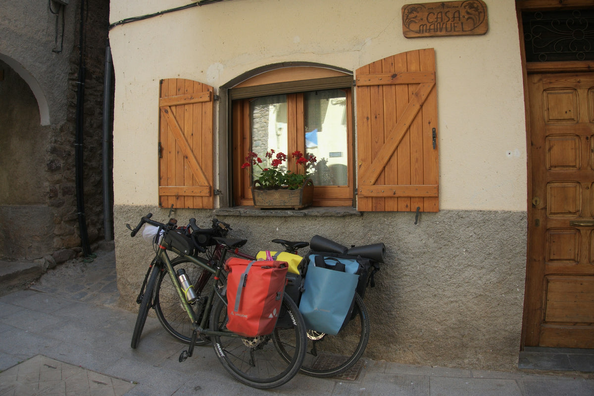 Zwei Reiseräder mit bunten Gepäckträgertaschen vor einem alten Haus mit Holzfensterläden